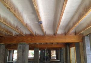 A man is spraying foam on the ceiling of a house under construction.