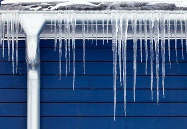Icicles are hanging from the gutter of a blue house.