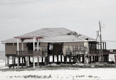 A black and white photo of a house on stilts on the beach.