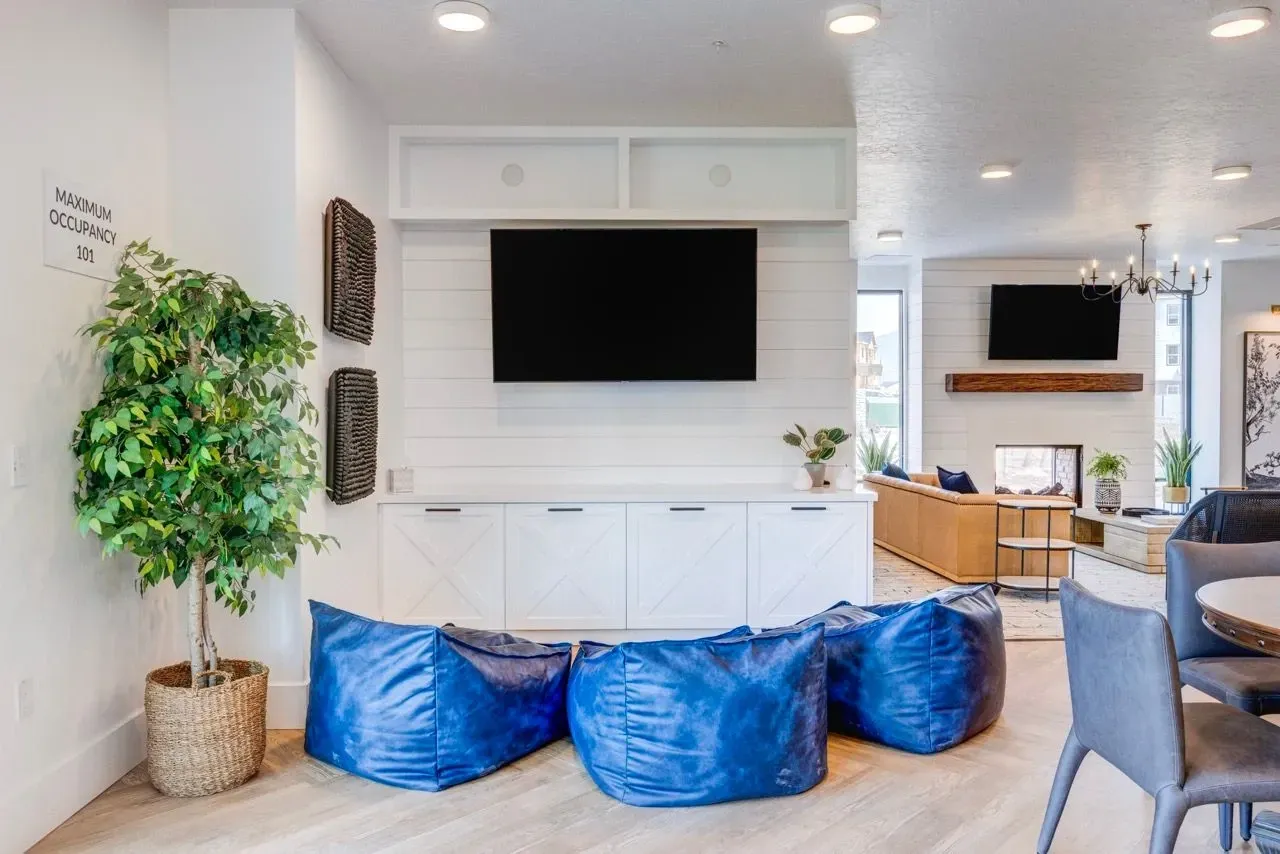 A modern communal lounge area with plush blue beanbag chairs and a large TV mounted on a white shiplap wall at Aria in Syracuse, UT.