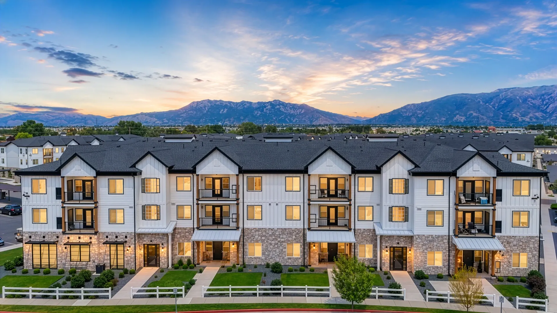 Modern apartment building exterior with balconies and mountain backdrop at sunset at Aria in Syracuse, UT.