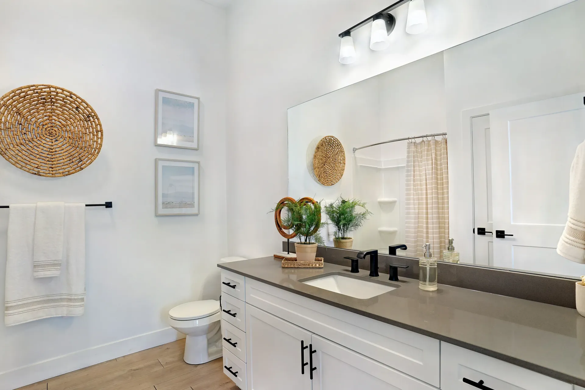 Modern bathroom with double vanity, large mirror, toilet, and decorative elements at Aria in Syracuse, UT.