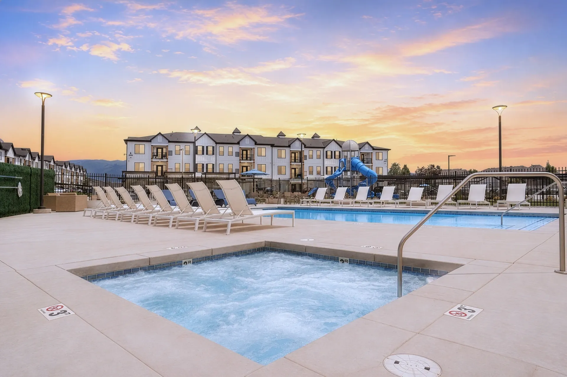 Community pool and hot tub area with lounge chairs and playground at Aria in Syracuse, UT.
