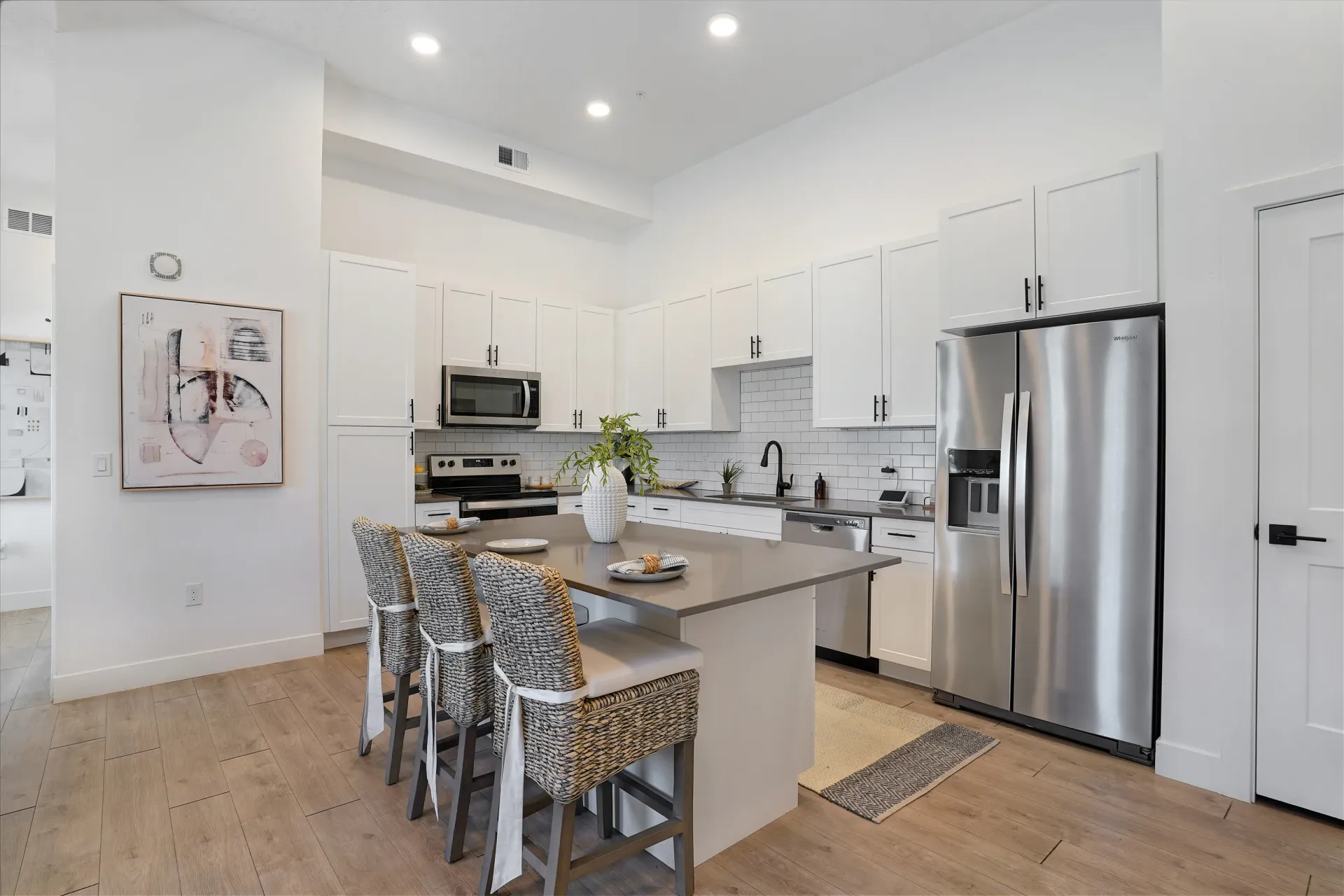 Modern kitchen with stainless steel appliances, white cabinetry, and a large island with bar stools at Aria in Syracuse, UT.