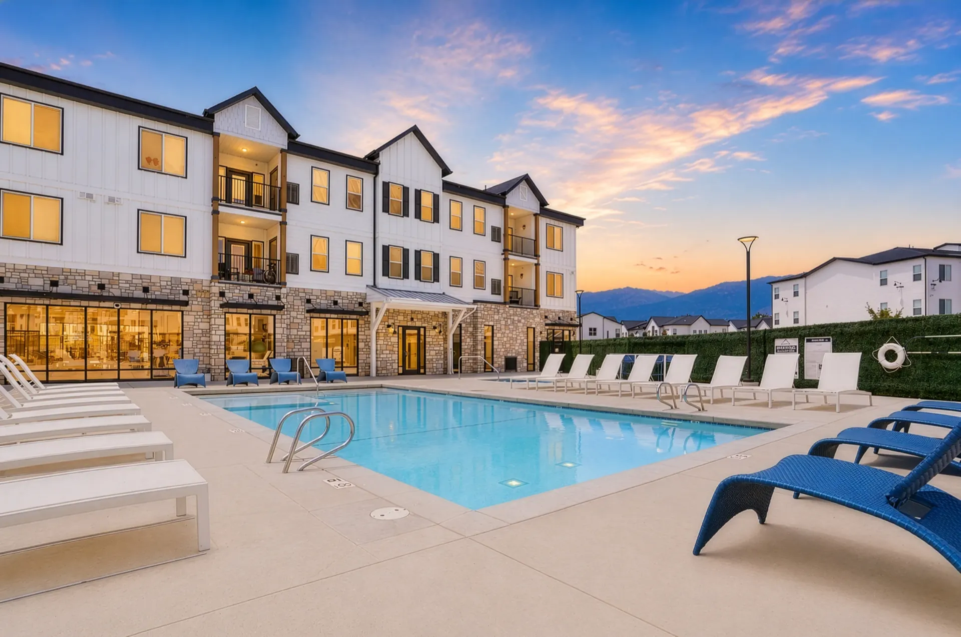 Resort-style swimming pool with lounge chairs and a modern apartment building at sunset at Aria in Syracuse, UT.