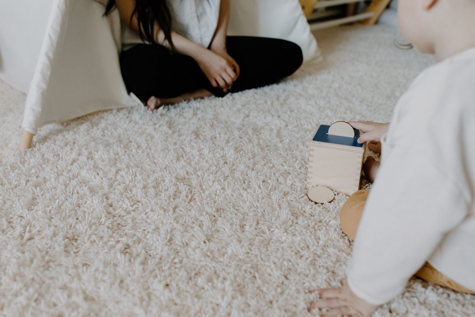Person playing with a small toy car on a fluffy carpet in a bright room