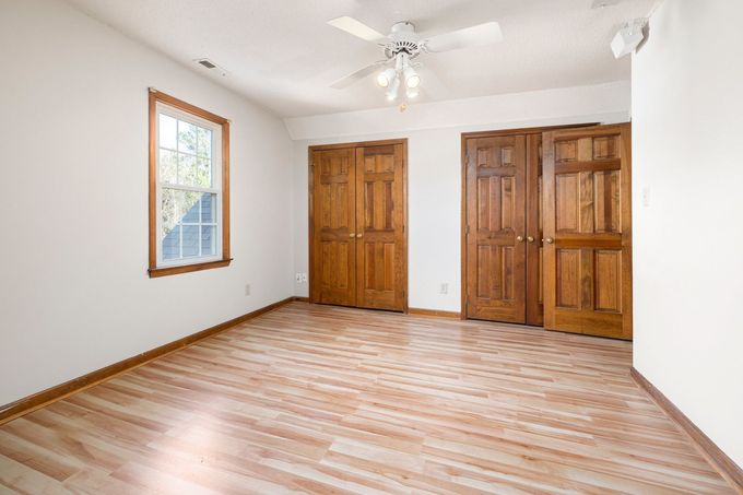 Empty bedroom with light wood floors, white walls, a window, and two wooden closets.