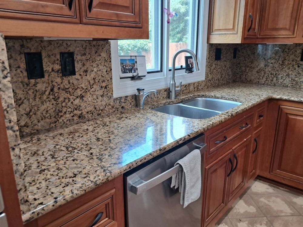 Granite kitchen countertop with sink, wooden cabinets, and a dishwasher below.