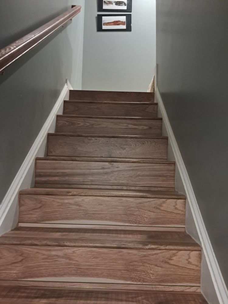 Narrow indoor staircase with wooden steps, gray walls, and a handrail on the left.