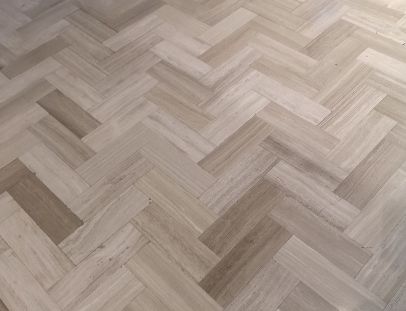 Light wood herringbone parquet flooring with varied beige and gray tones