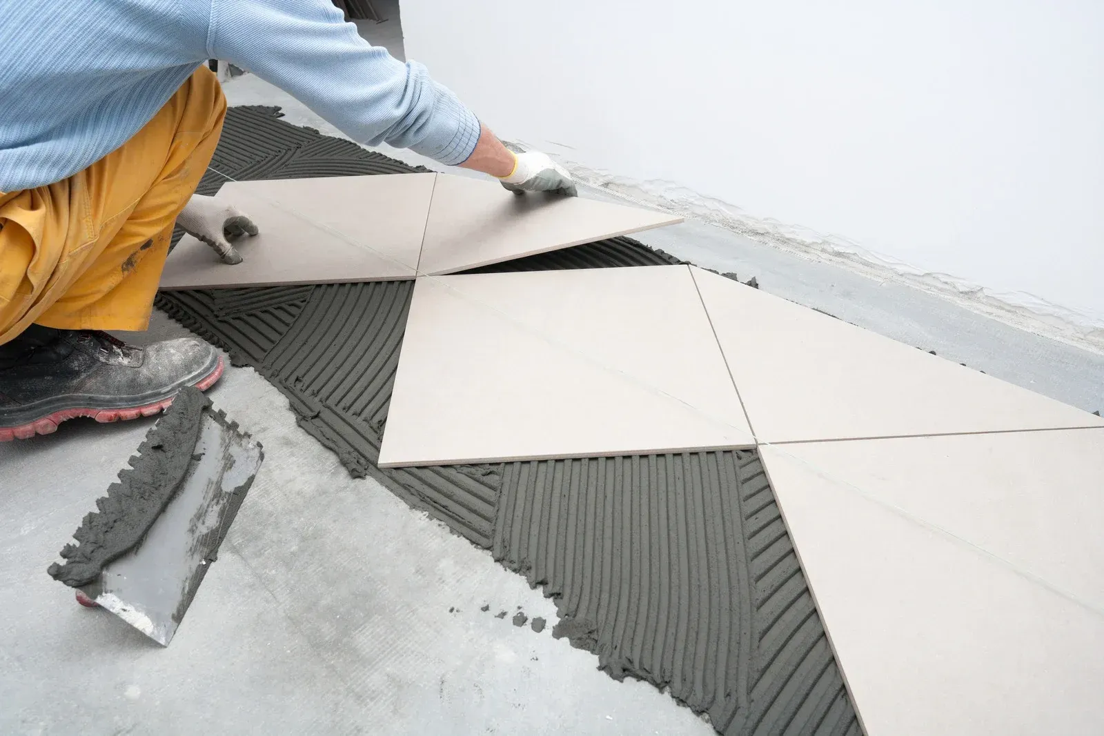 Worker laying large white tiles over gray adhesive on a floor under construction