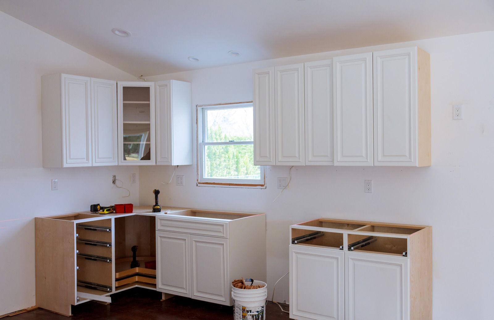 Partially renovated kitchen with white cabinets and open drawers under a window