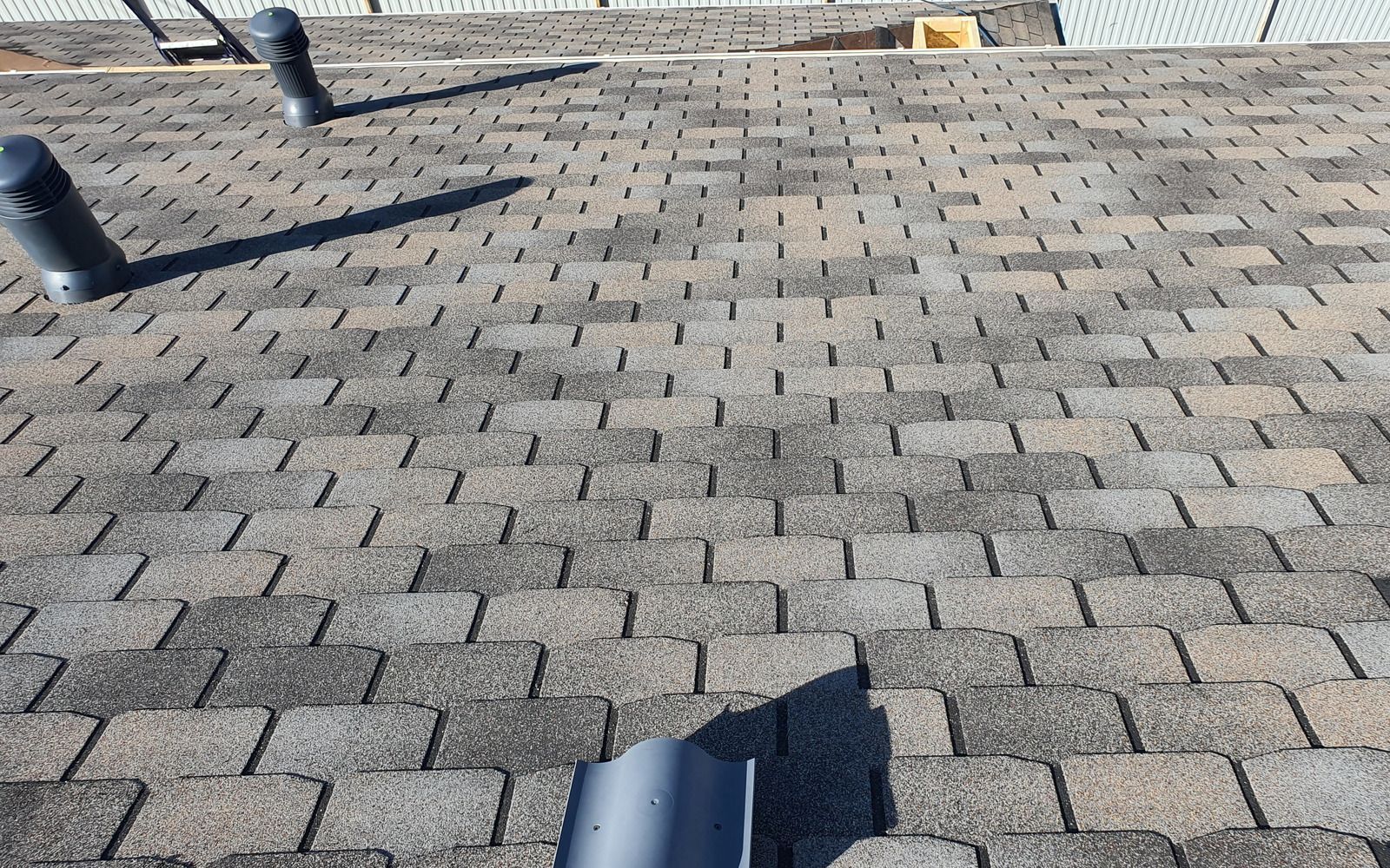 Shingled rooftop with two black vent pipes and blue sky at the top edge