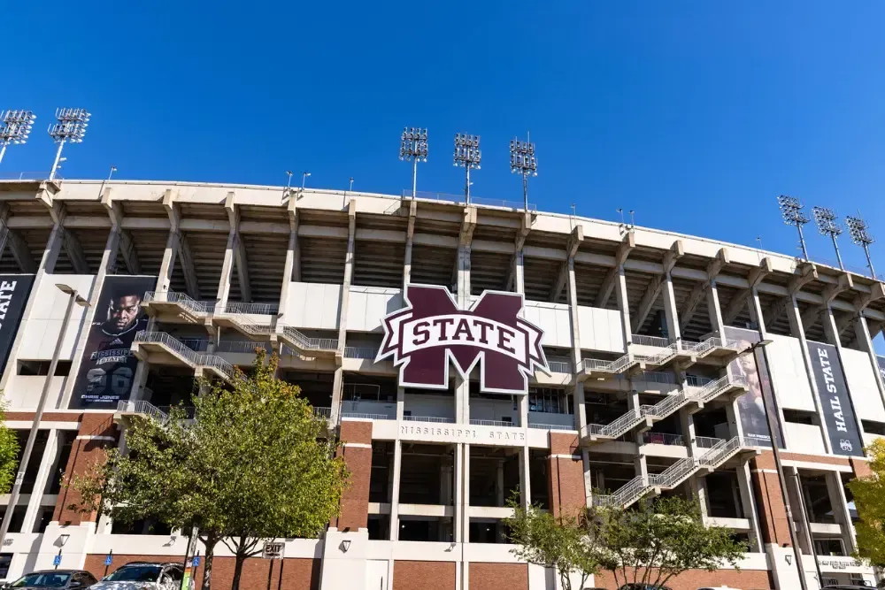 Mississippi State stadium exterior with maroon “STATE” sign and stadium lights under a blue sky