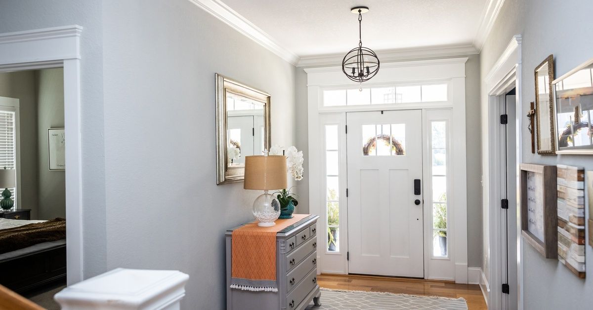 A gray entry hall leads to a white front door with glass sidelights, a wood floor, and a small side table.