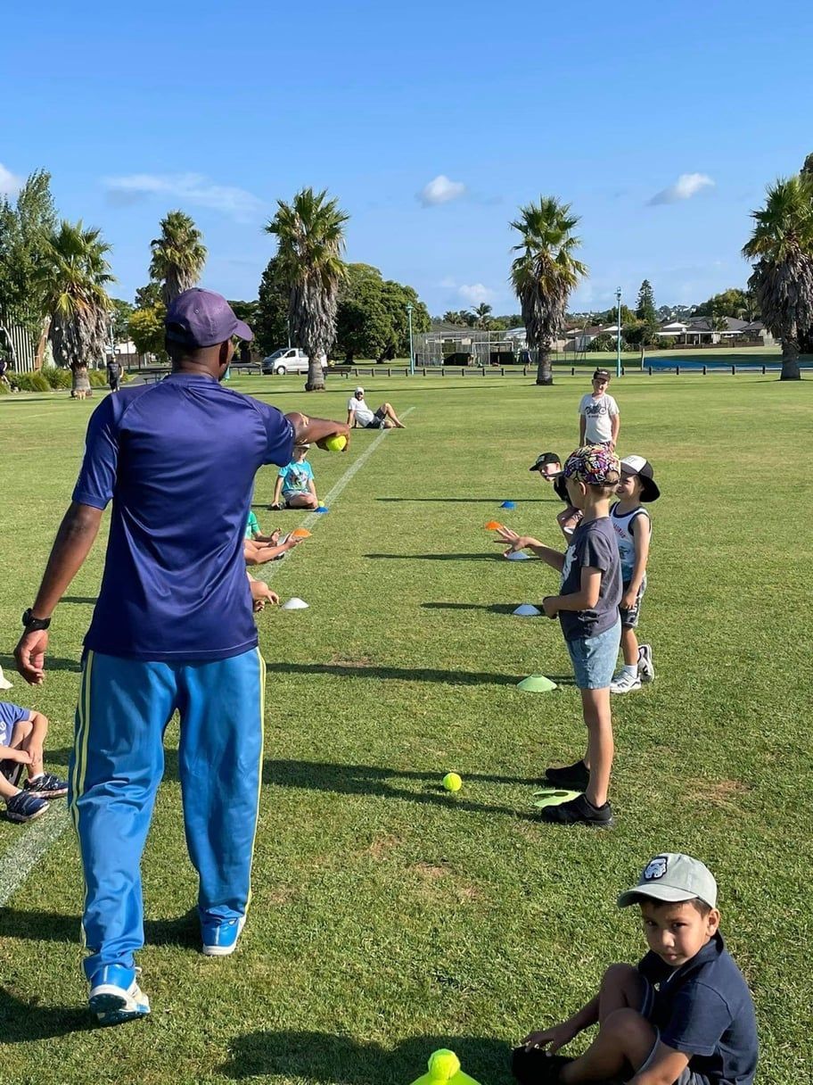 People playing a ball game on a sunny field with cones and scattered balls near palm trees
