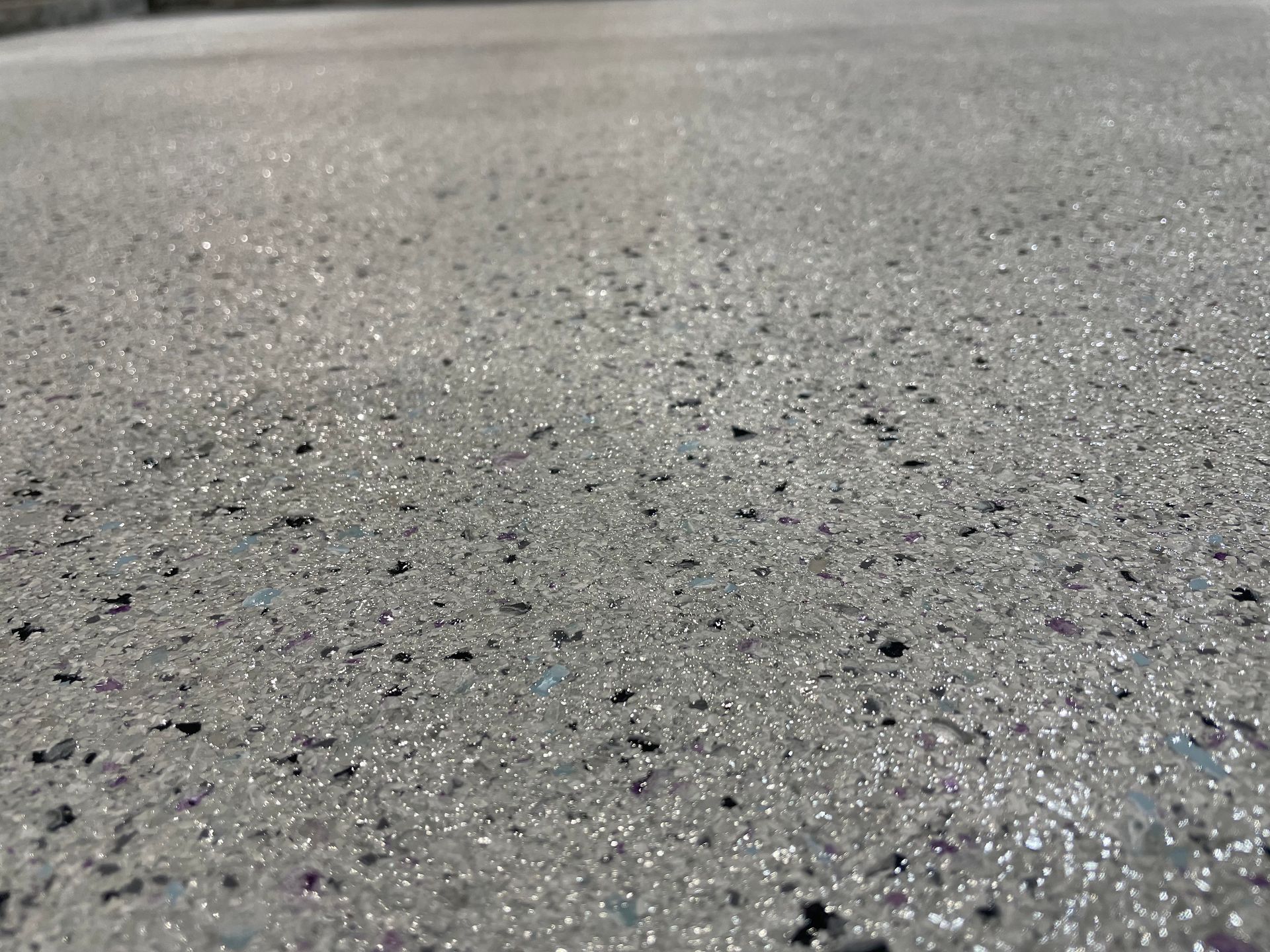 Close-up of wet, textured pavement with small dark specks and a gray background.