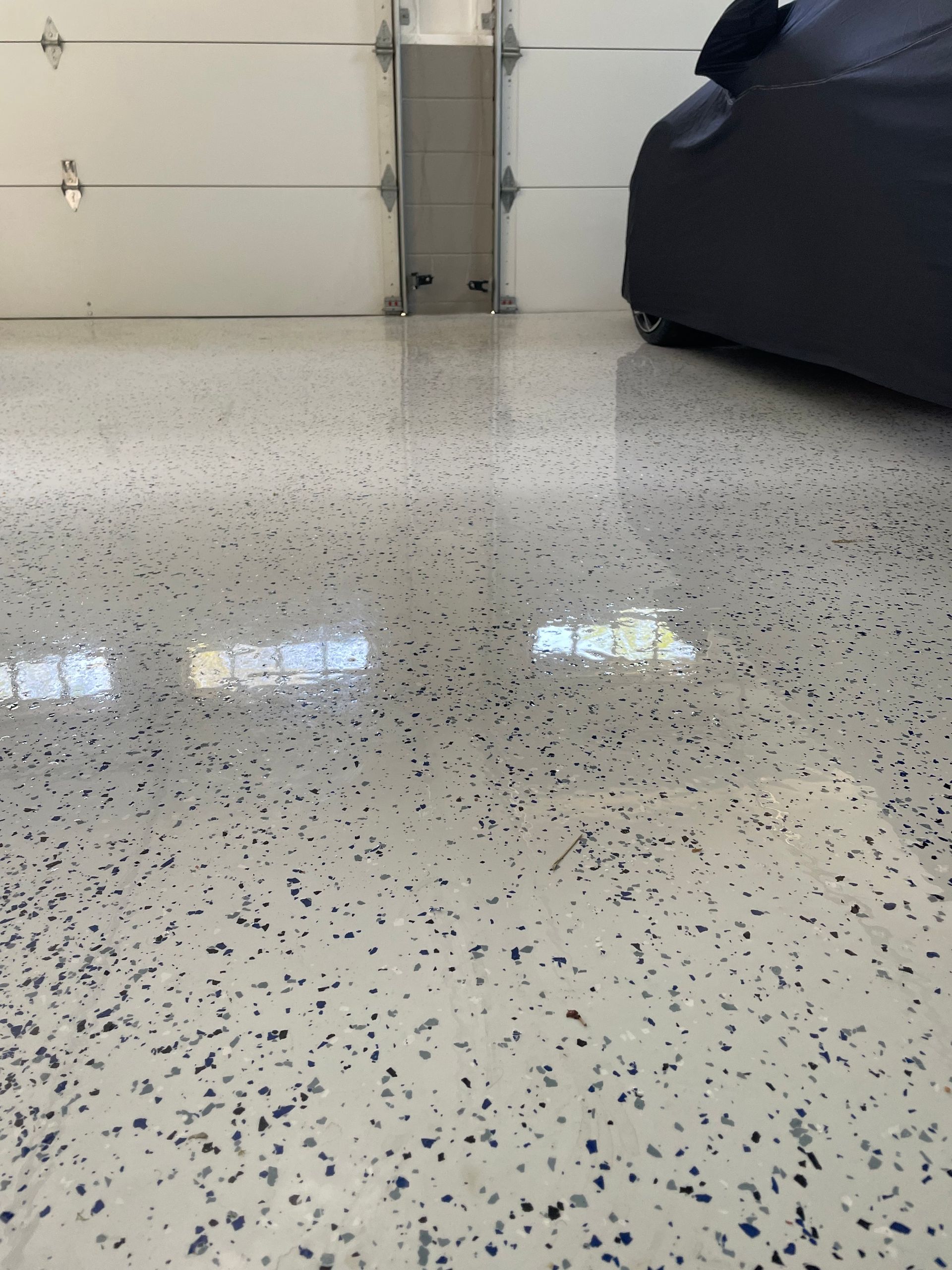 Speckled epoxy garage floor with a closed white door and a covered vehicle on the right