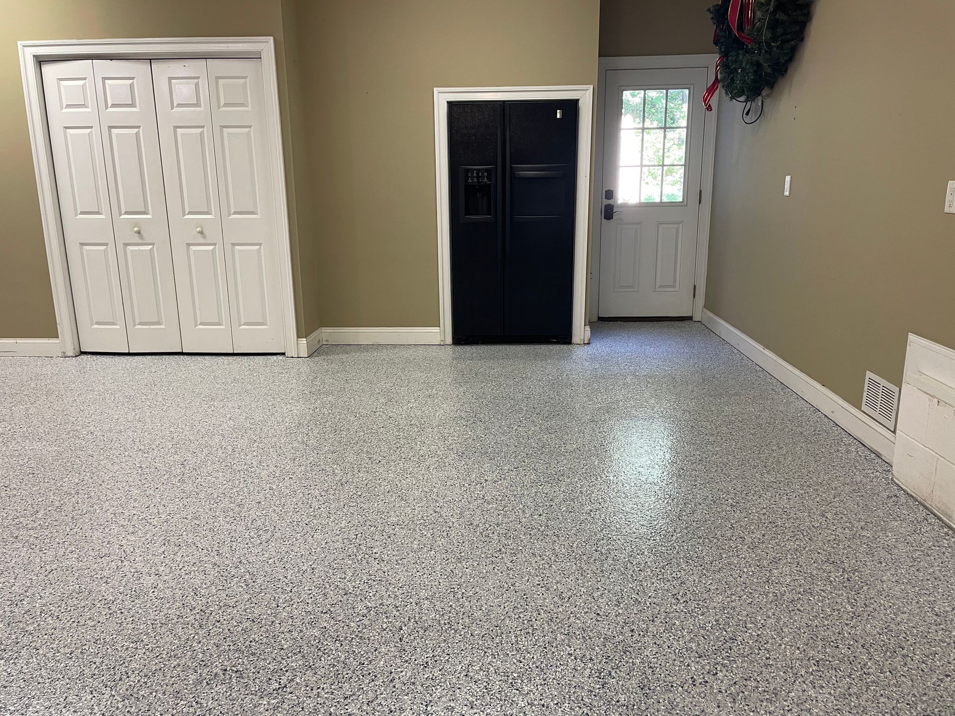 Empty room with speckled floor, beige walls, double white closet doors, and a black refrigerator near the back wall