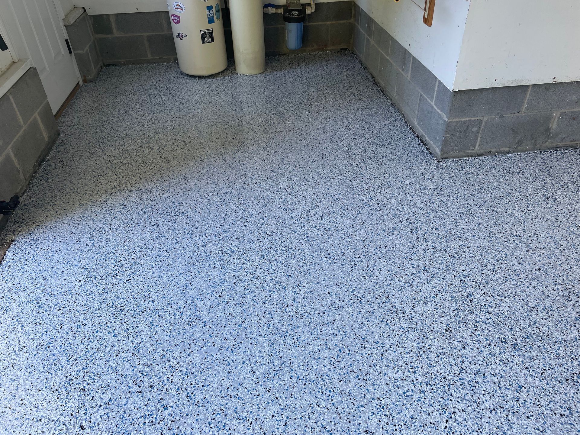 Speckled gray floor in a small indoor room with white and gray walls and cleaning bins in back