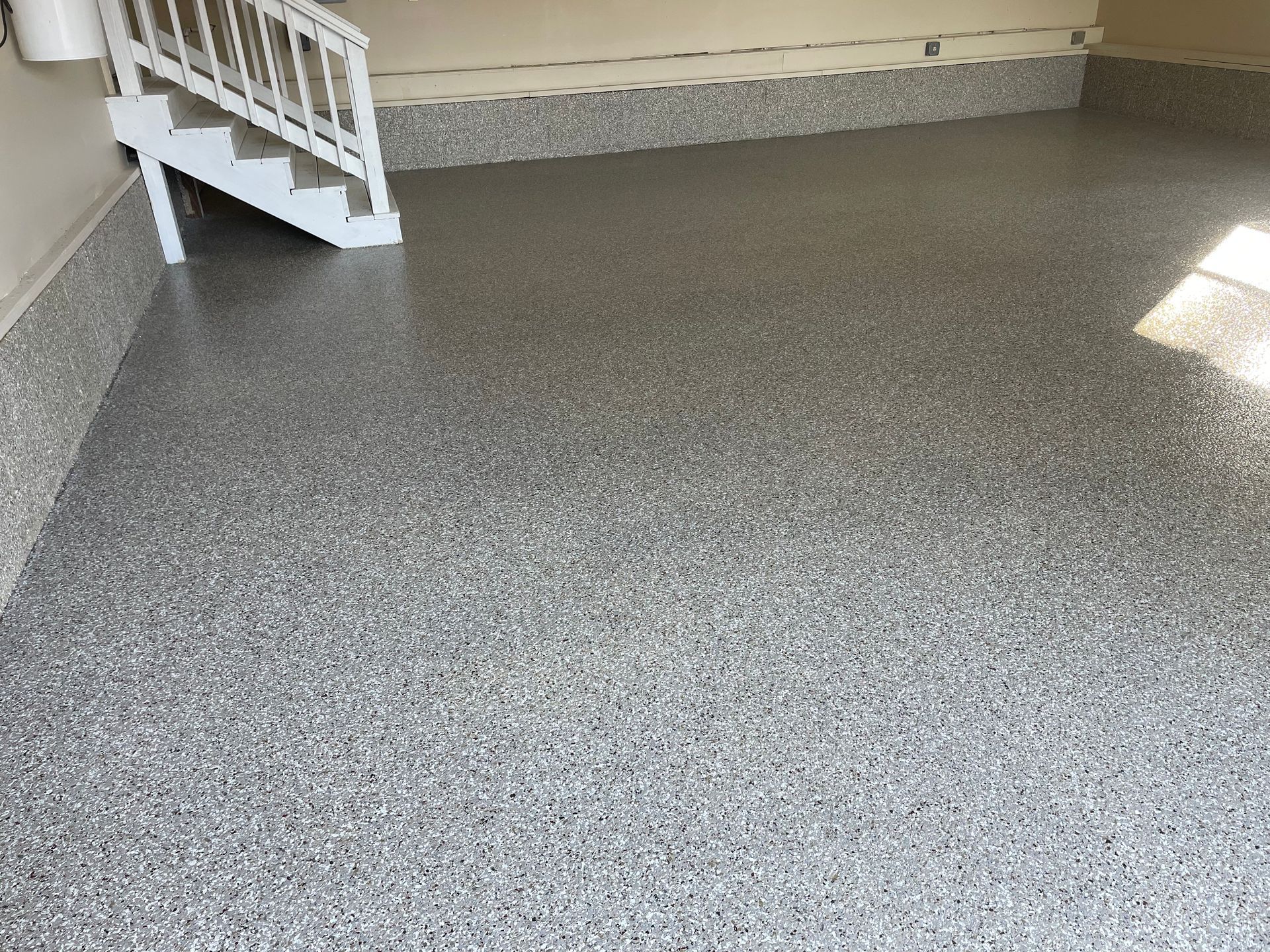 Empty gray-speckled floor in a covered porch or garage, with white stairs at left.