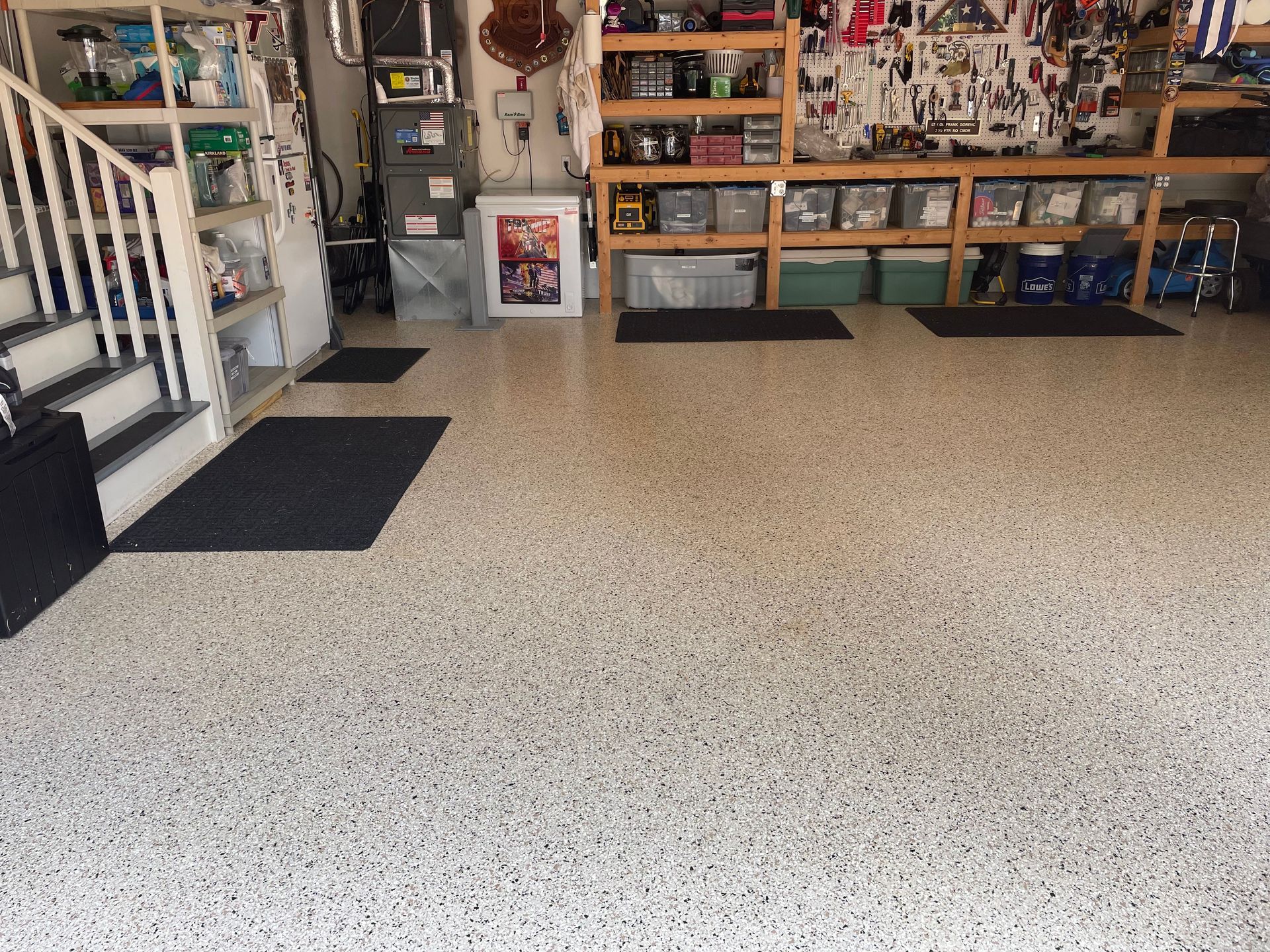 Garage with speckled epoxy floor, stairs on the left, and shelves and cabinets along the back wall.