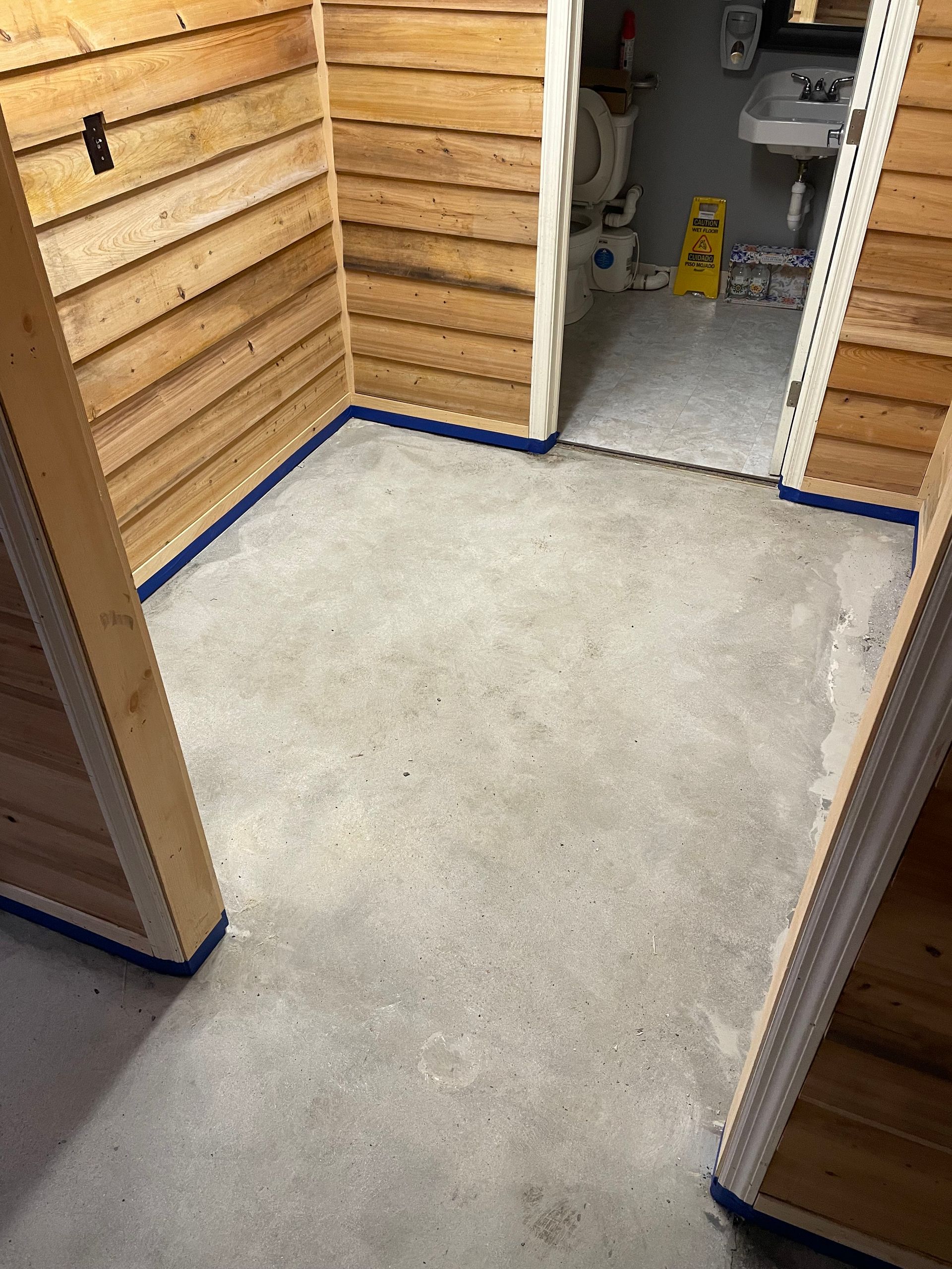 Empty concrete hallway with wood-paneled walls and an open doorway to a utility room.