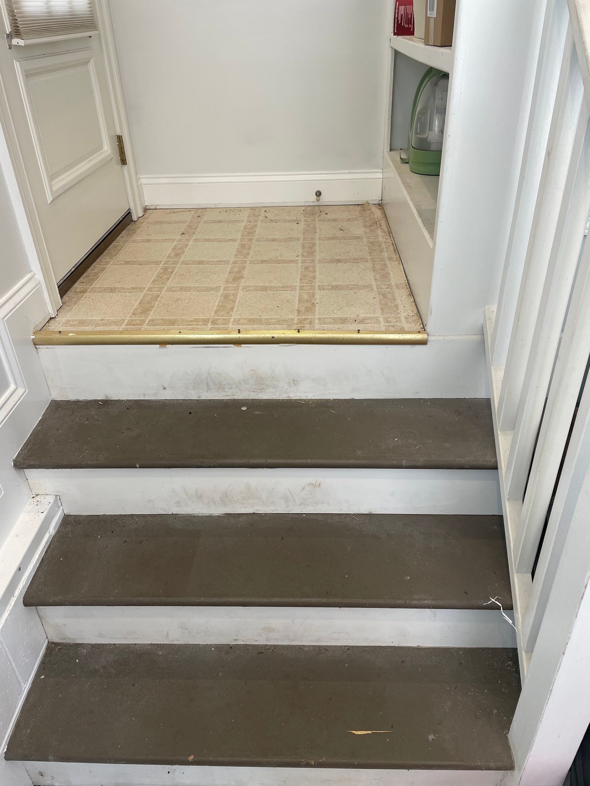Three carpeted steps leading to a small tiled landing between white walls and a closet area