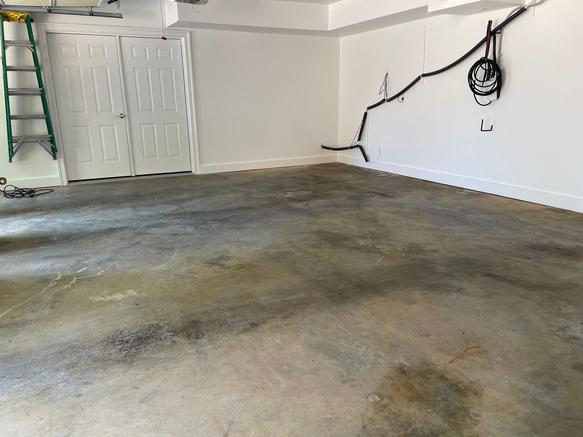 Empty garage with stained concrete floor and white walls, cable hanging on the right side.
