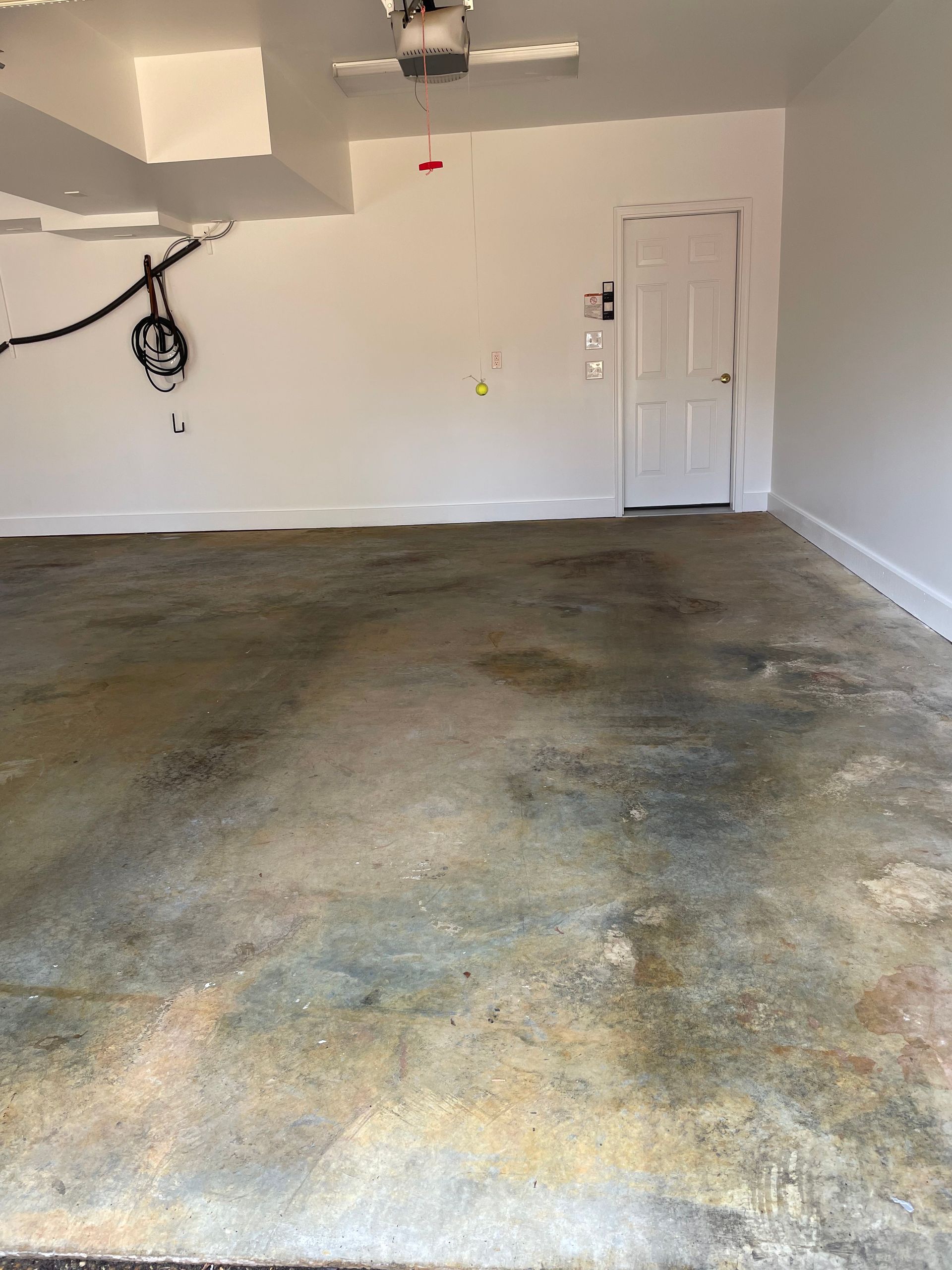 Empty garage with stained concrete floor, white walls, ceiling opener, and closed side door