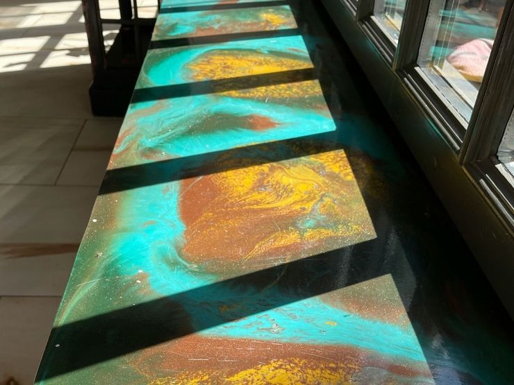 Sunlit walkway with colorful turquoise and orange stained-glass panels casting patterns on the floor