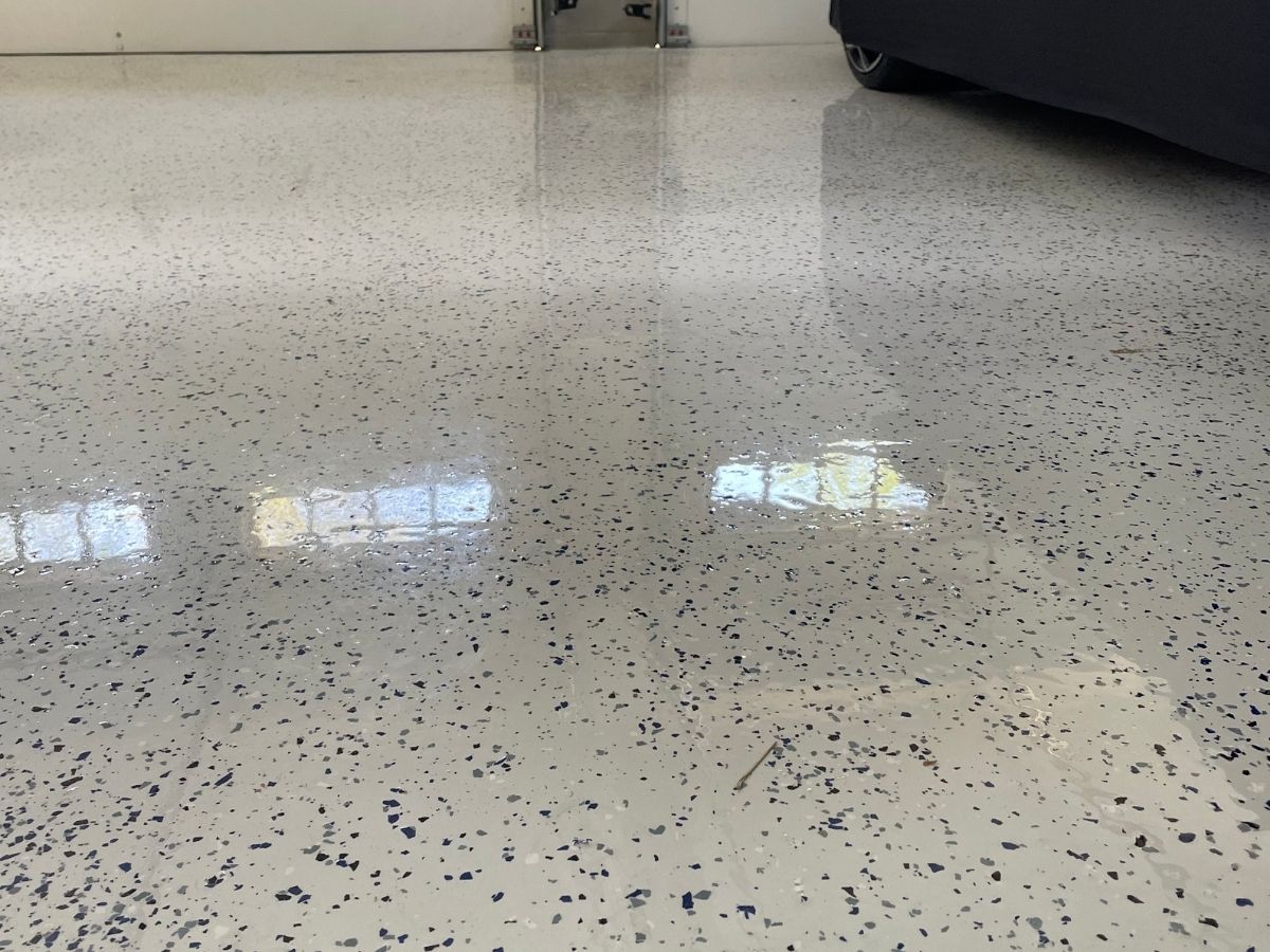 Speckled gray floor with reflections of windows and a dark object at the right edge