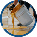 Worker tipping white paint bucket, spilling orange paint onto a floor