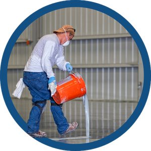 Worker in safety gear pouring liquid from an orange bucket in an industrial facility