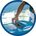 Hand smoothing blue surfboard wax with a small scraper near the water