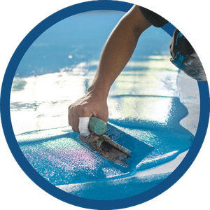 Hand smoothing blue surfboard wax with a small scraper near the water