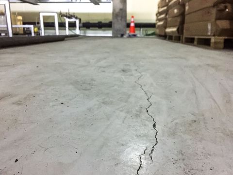 Cracked concrete warehouse floor with stacked pallets and a traffic cone in the background