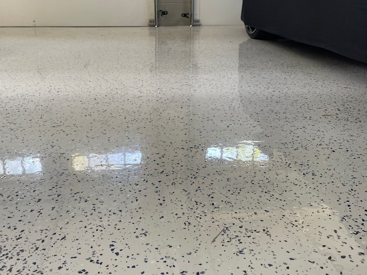 Speckled white floor with reflections, near a dark sofa and wall baseboard