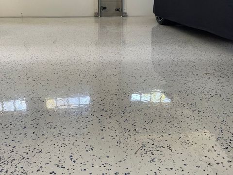 Speckled white floor with reflections, near a dark sofa and wall baseboard