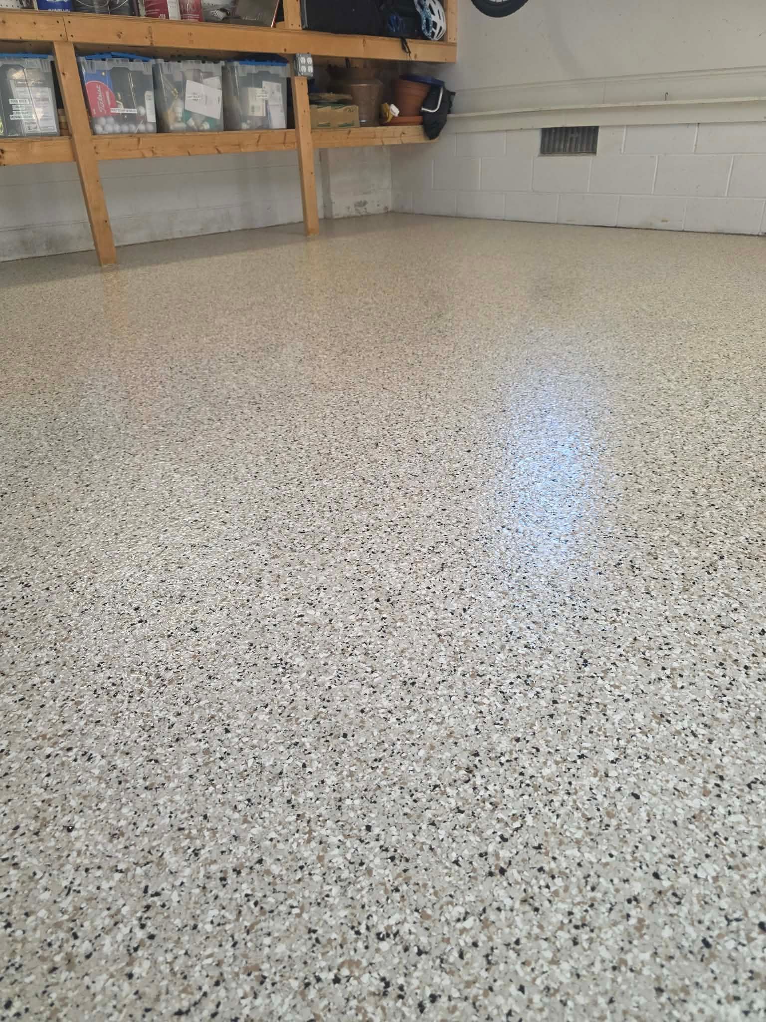 Speckled epoxy garage floor beneath a wooden shelf and cinderblock wall, with a bright window reflection