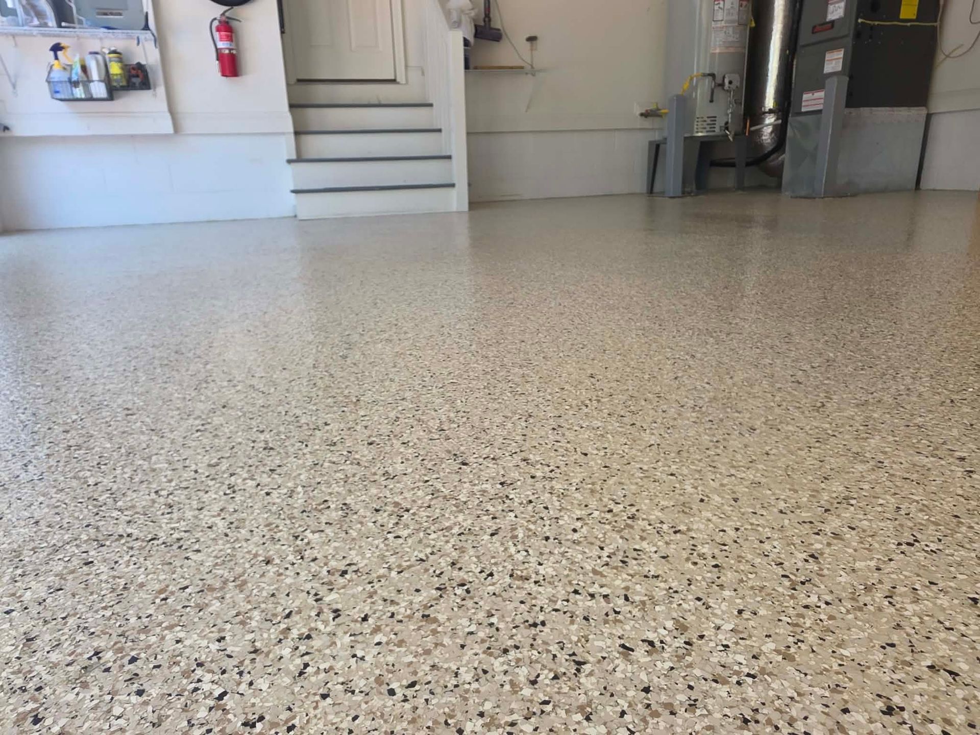 Empty speckled floor in a bright indoor room with stairs and utility cabinets in the background