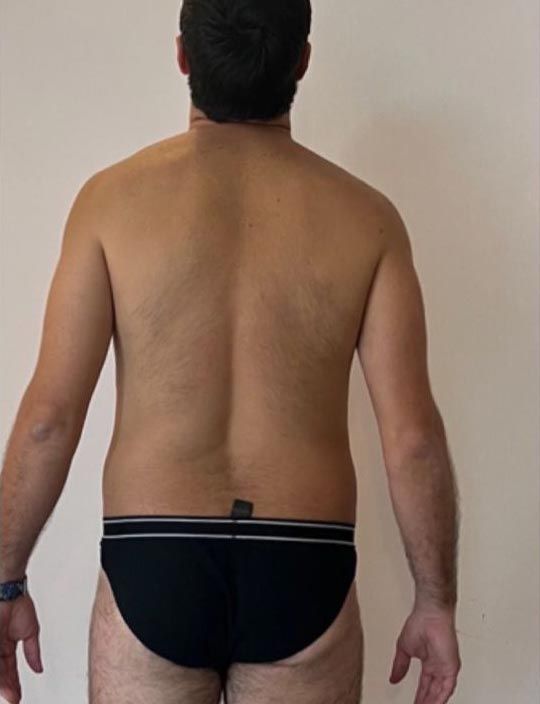 Un uomo a torso nudo, in mutande nere, è in piedi davanti a un muro bianco.