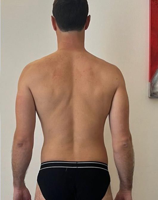 Un uomo a torso nudo, in mutande nere, è in piedi davanti a un muro.