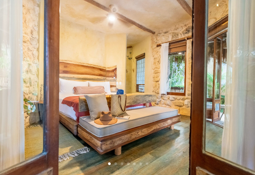 Bedroom with a wooden bed frame, stone walls, and doors leading to a veranda with greenery.