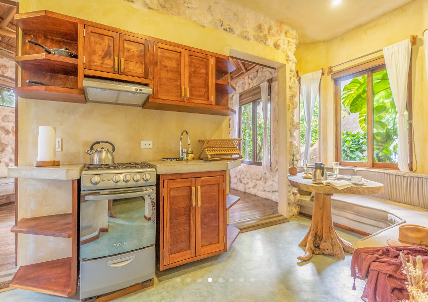 Kitchen with wooden cabinets, a stove, and stone walls. Light floods in from windows.