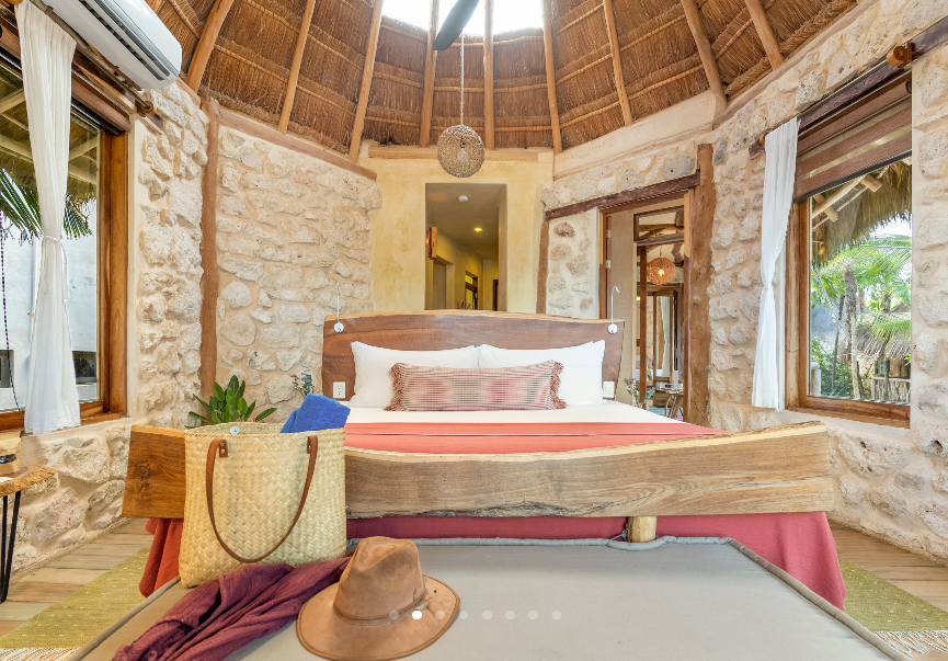 Bedroom with stone walls, wooden bed frame, thatched ceiling, and natural light.