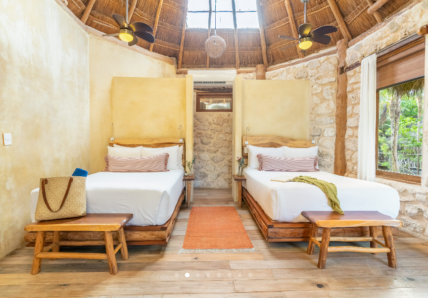 Two twin beds in a rustic room with a thatched roof, wooden accents, and a small rug.