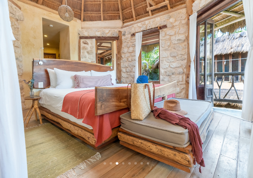 Bedroom with stone walls, thatched roof, wooden bed and daybed, open to a balcony.