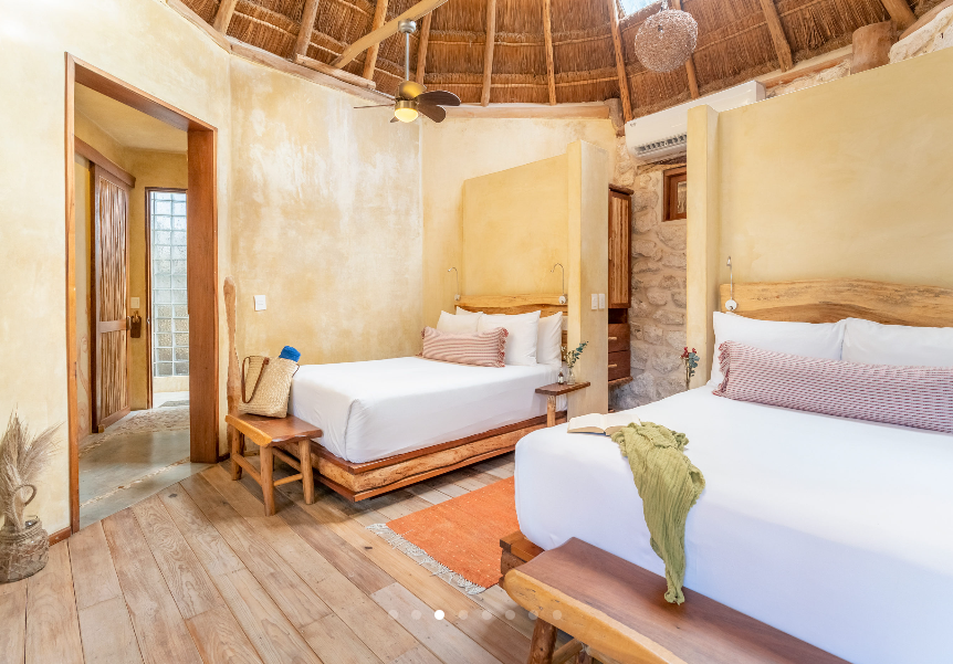 Bedroom with two beds, thatched roof, wood floors, and open door.