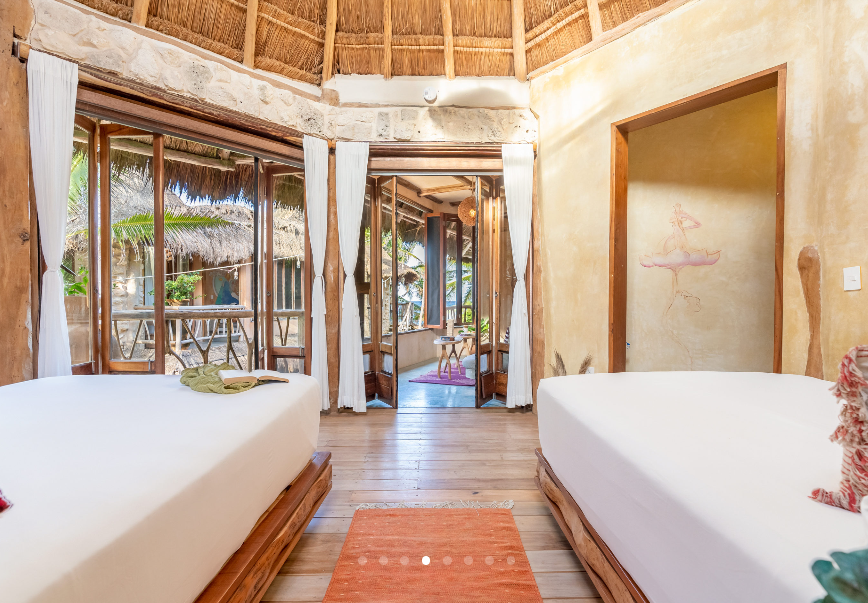 Spa interior with two massage tables, open doors, and a thatched roof.